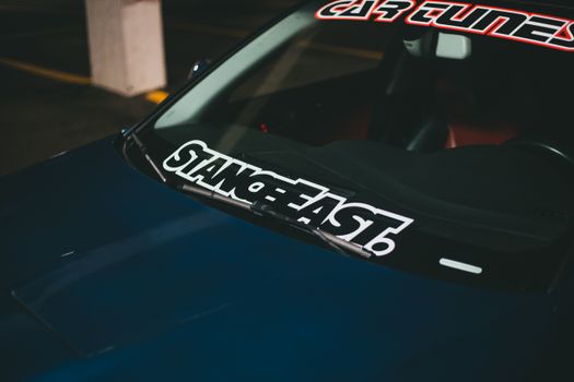 Dark blue sports car focus on windshield stickers in dimly lit setting, emphasizing style and details.