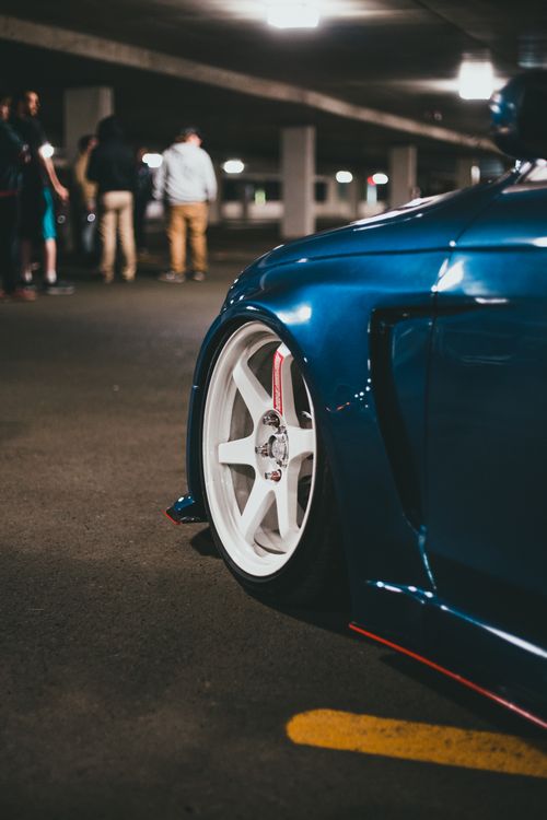 Free Close-up of a blue car's wheel in an underground parking garage with people in the background. Stock Photo