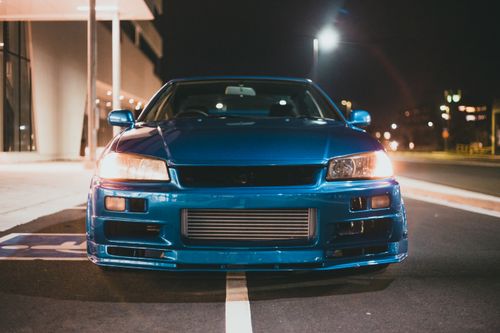 Free Front view of a sleek blue sports car parked on a city street at night, showcasing its modern design. Stock Photo
