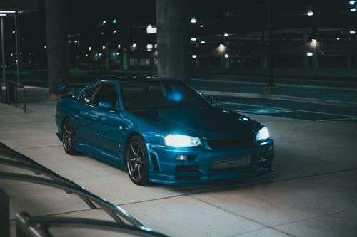 Free A blue sports car with shining headlights parked in an urban area at night, showcasing modern design and style. Stock Photo