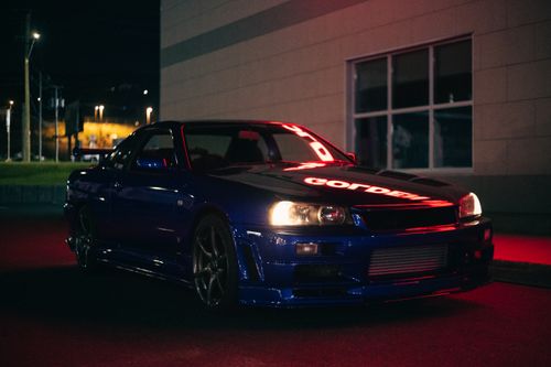 Free A sleek blue sports car parked at night, illuminated by red neon lights and city background. Stock Photo