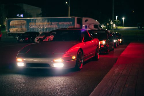Free A line of sleek sports cars parked on a dimly lit street at night, creating a moody urban scene. Stock Photo