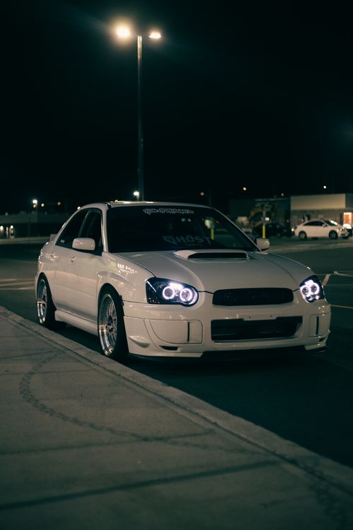 Free A sleek white sports car parked in a dimly lit urban area at night, showcasing automotive design. Stock Photo