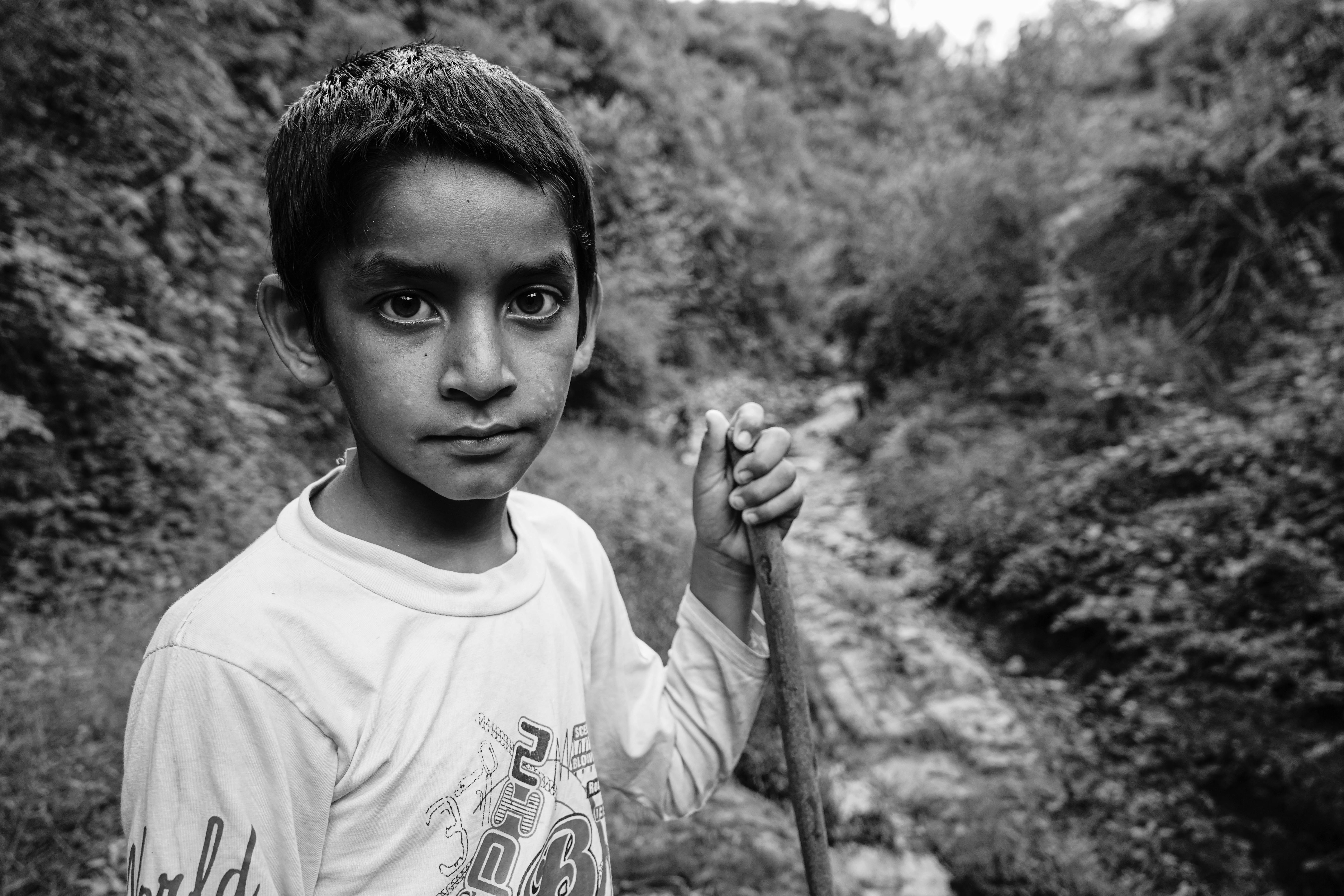 Grayscale Photo of Boy in Crew Neck T-shirt Holding Stick · Free Stock