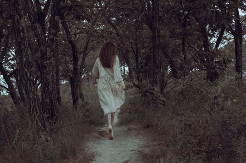 Free A woman in a white dress runs barefoot through a mysterious and enchanting forest path. Stock Photo