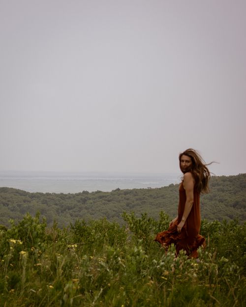 Free A woman in a flowing brown dress stands on a hilltop, gazing at a scenic landscape. Stock Photo