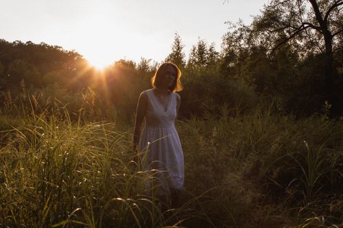 Free A woman in a white dress enjoying a sunlit walk in a grassy field. Stock Photo