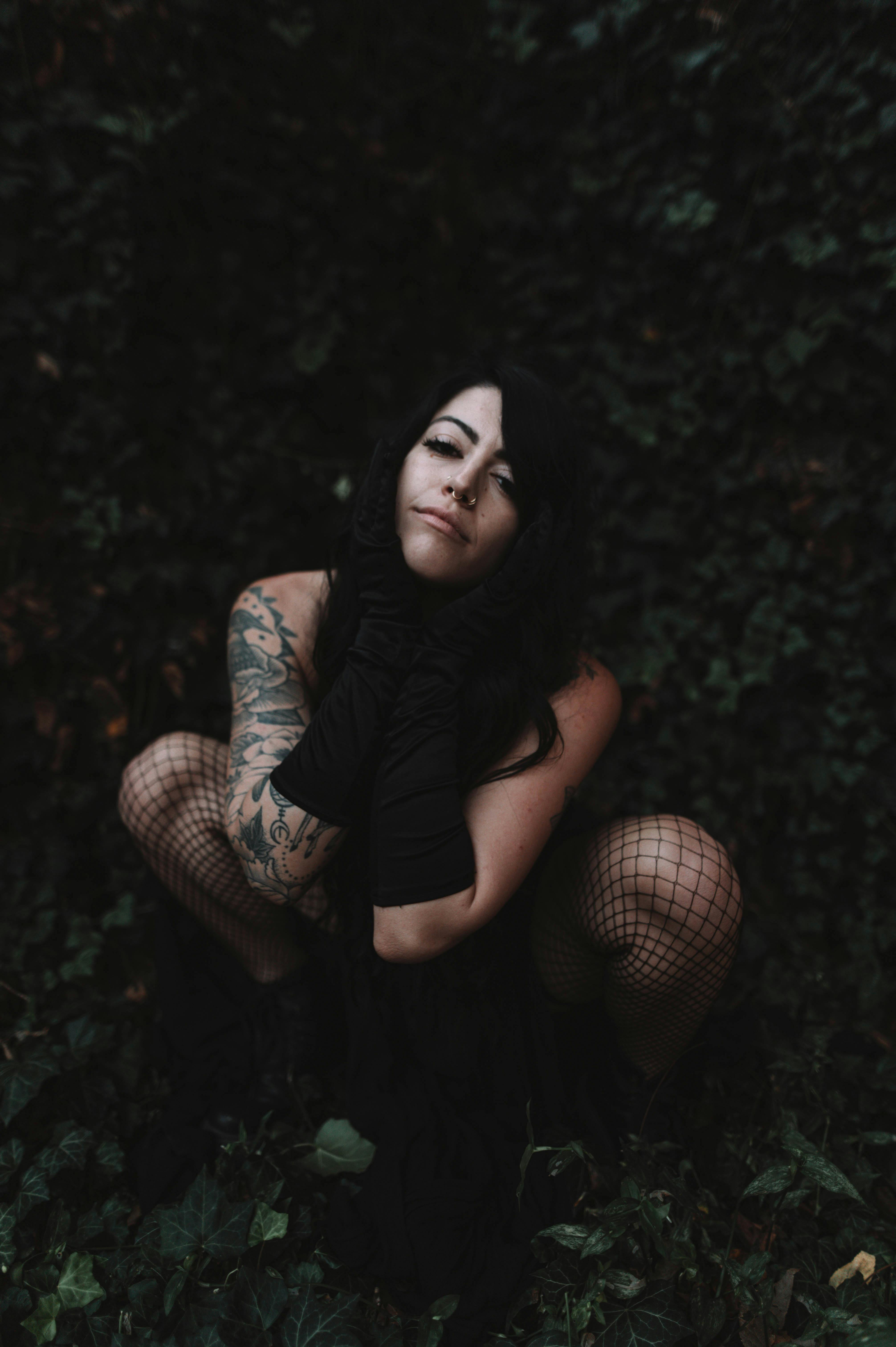Stylish model in black dress and gloves with tattoos posing outdoors.