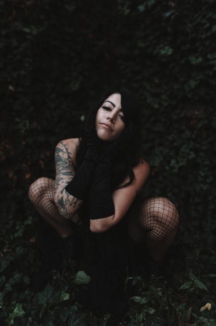 Stylish model in black dress and gloves with tattoos posing outdoors.