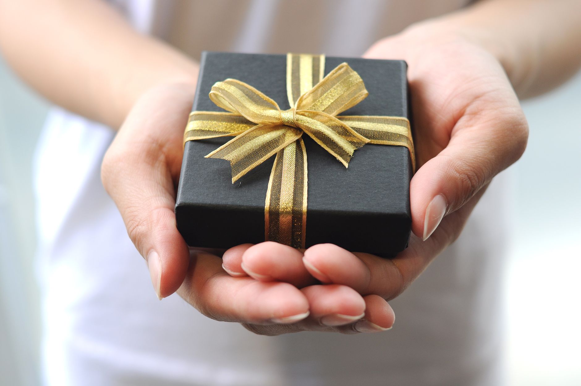A person holds a black gift box tied with a golden ribbon, symbolizing celebration and generosity.