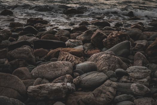 Dark and moody coastal scene of eroded rocks and waves on the shoreline.