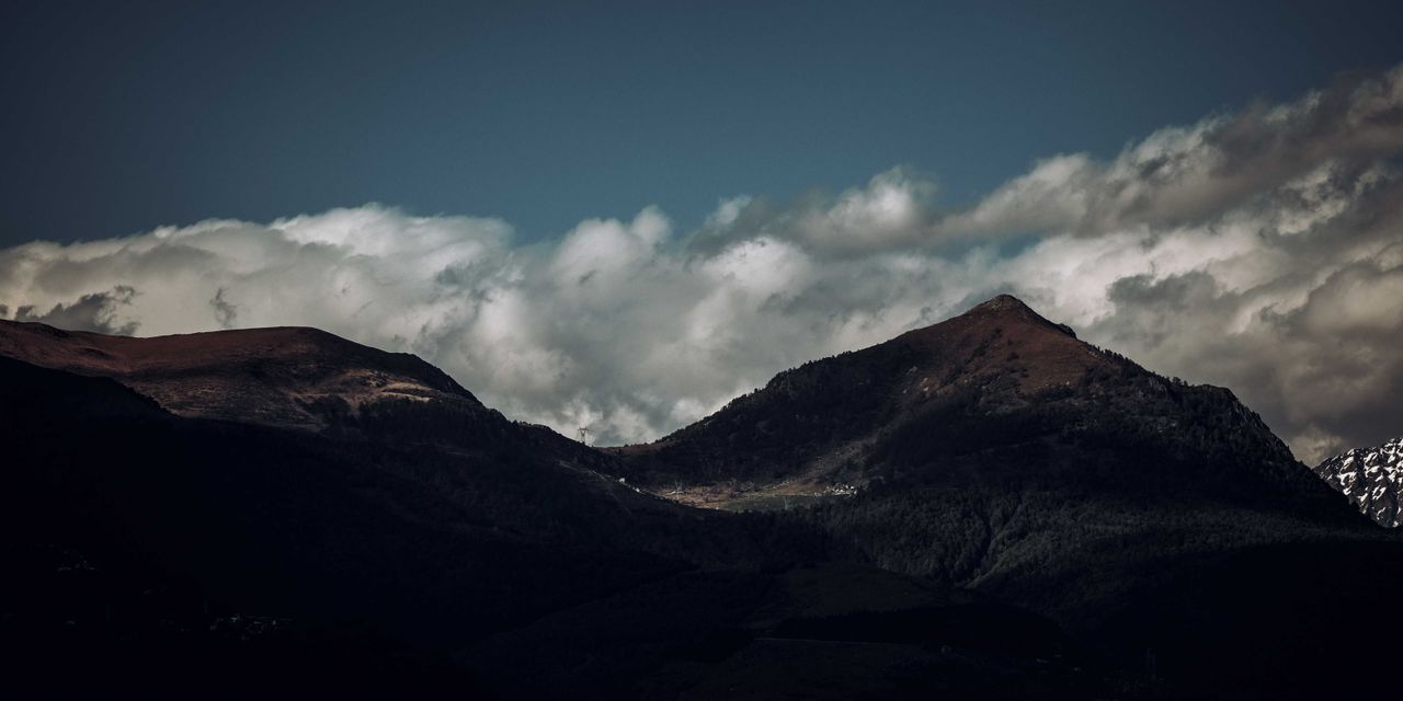 A dramatic mountain landscape beneath a moody sky with white clouds.