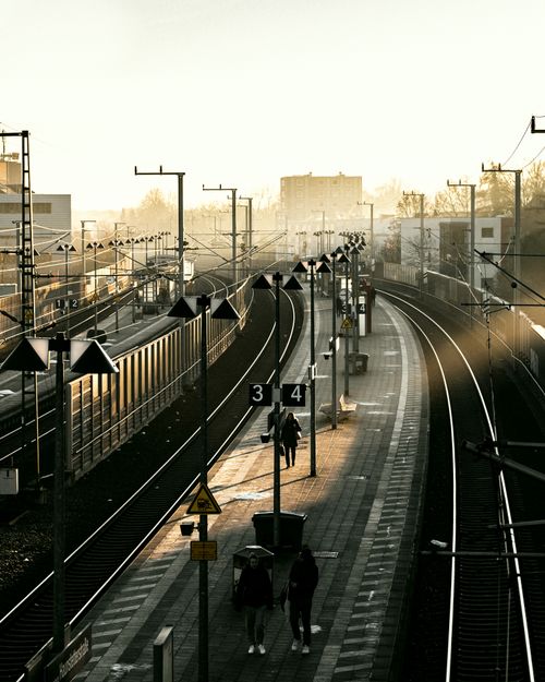 Free A sunlit railway station with curved tracks, featuring a few people walking on the platform. Stock Photo