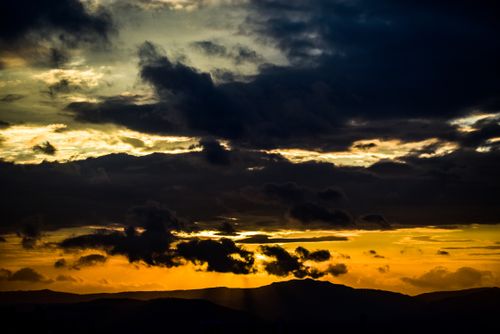 Free A stunning sunset with rich clouds over hilly terrain, creating a dramatic and moody atmosphere. Stock Photo