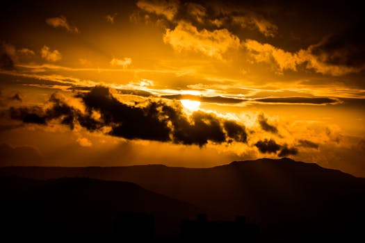 Dramatic sunset with sun rays piercing dark clouds over mountain silhouettes.