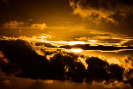 Captivating sunset with sun peeking through dramatic clouds during golden hour.