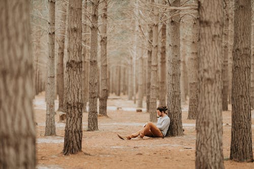 Adult man sitting by tree in forest and looking down