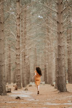 A woman in an orange dress runs through a serene pine forest, embracing nature.