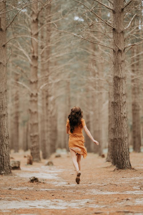 Adult woman running in dress among trees