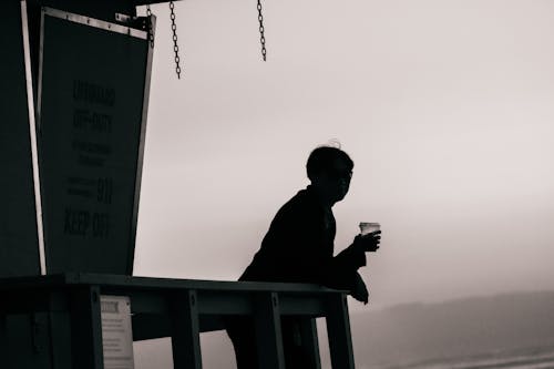 Silhouette of a Person Holding a Beverage while on a Lifeguard Tower