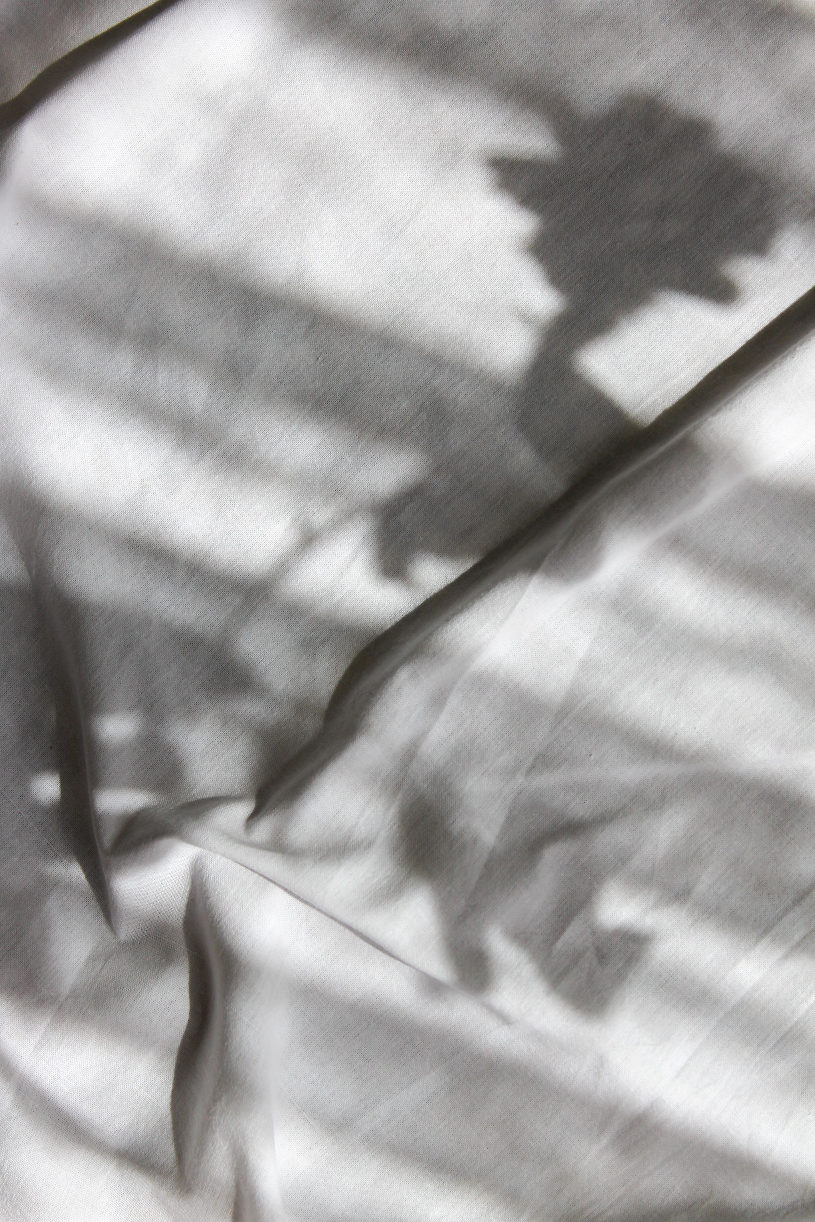 Abstract shadow patterns cast on white fabric creating intriguing visual textures.