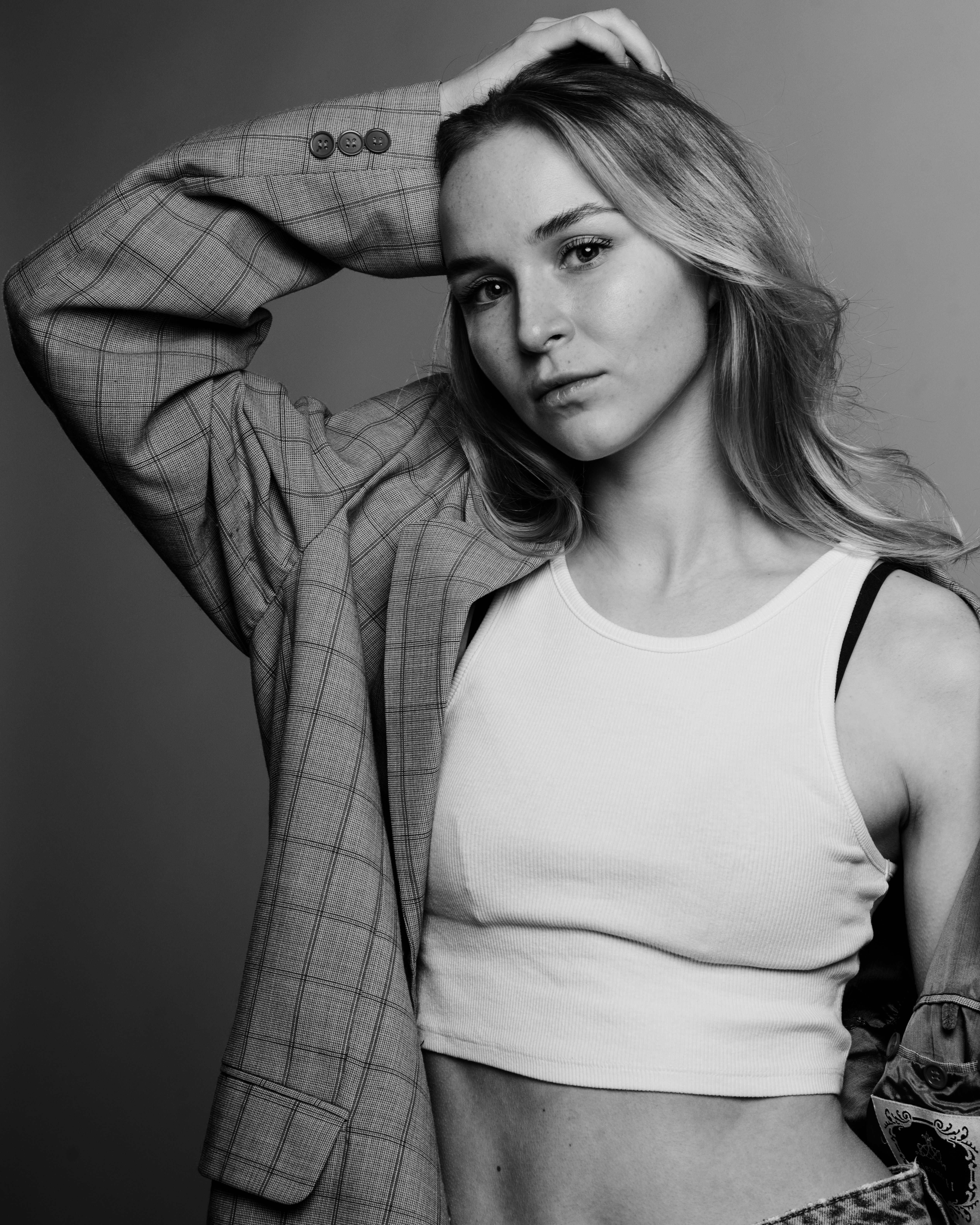 Black and white portrait of a woman in a plaid blazer and crop top posing confidently.