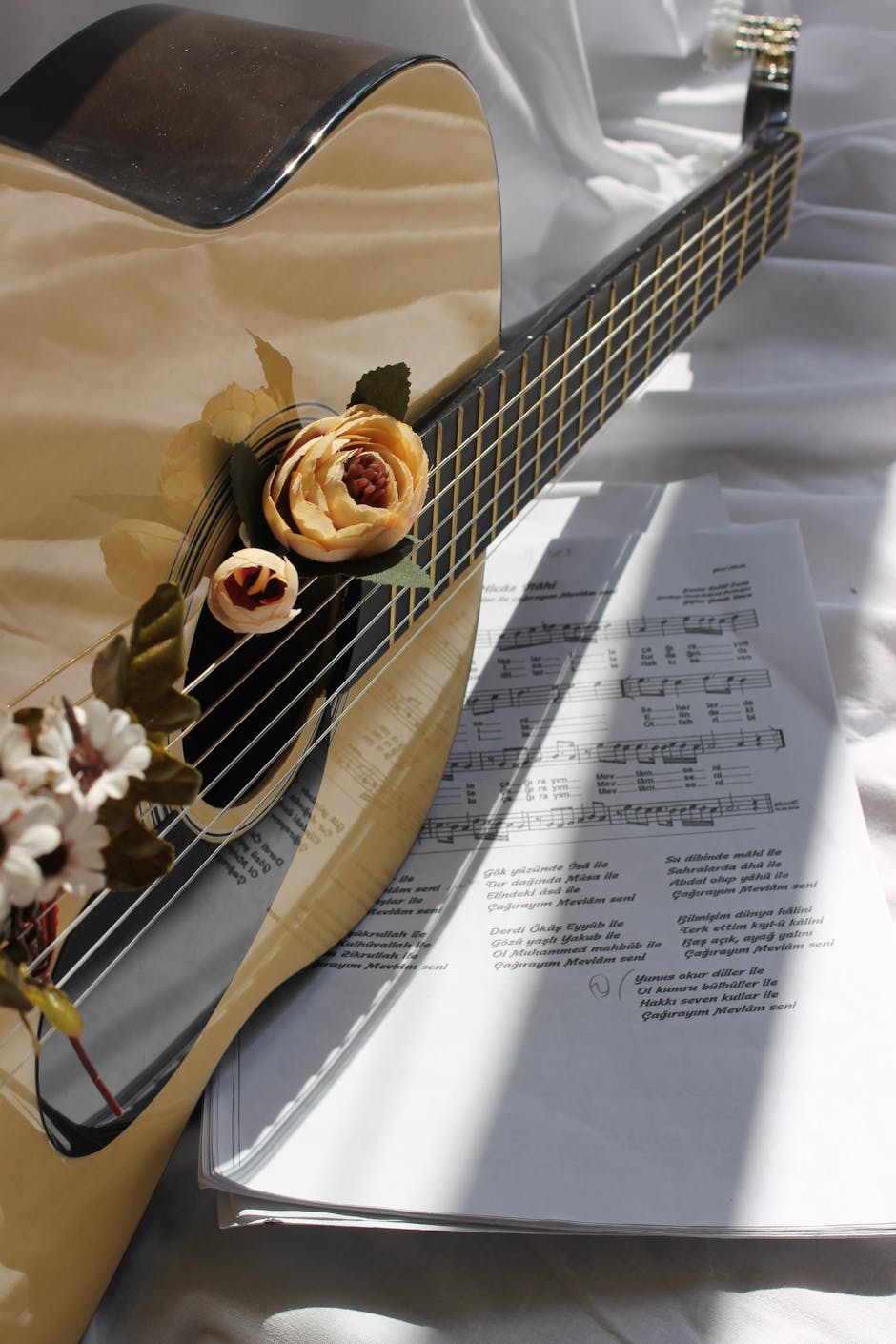 A close-up of a guitar adorned with flowers and sheet music in natural light.