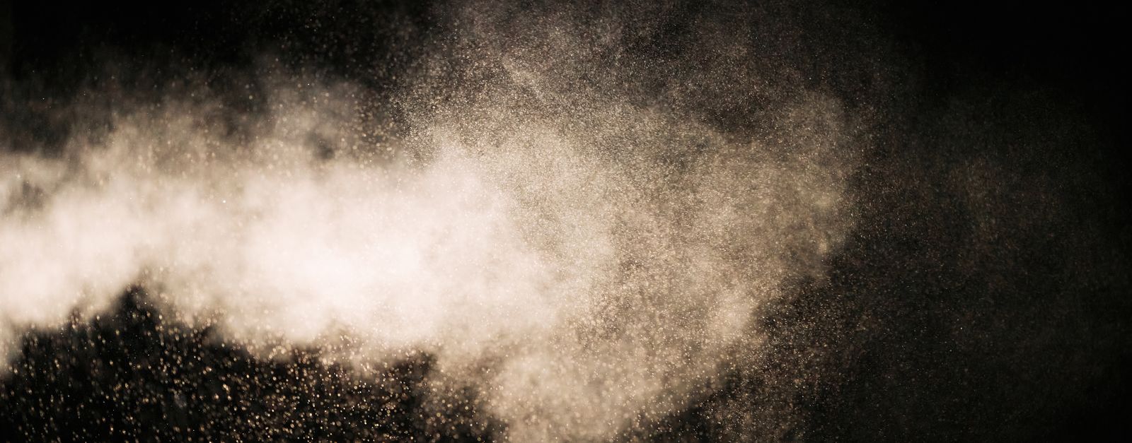 Dynamic view of dust particles in motion, illuminated against a black background, creating an ethereal effect.