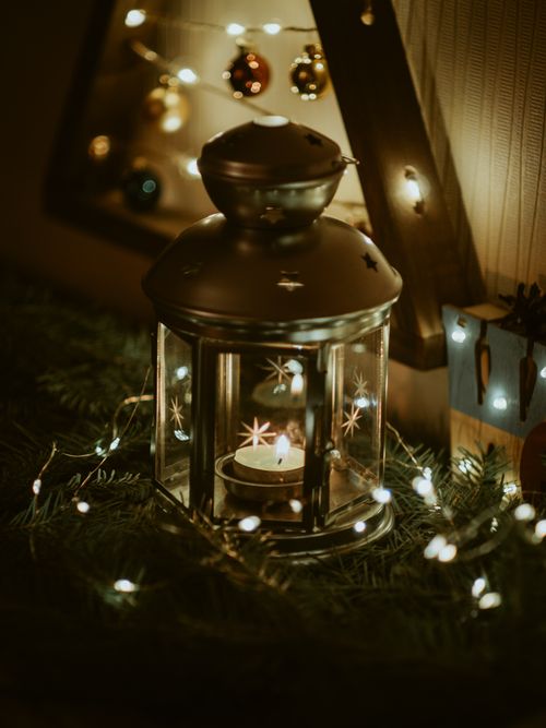Free Warm candlelit scene with a lantern, fairy lights, and Christmas ornaments on a conifer wreath. Stock Photo