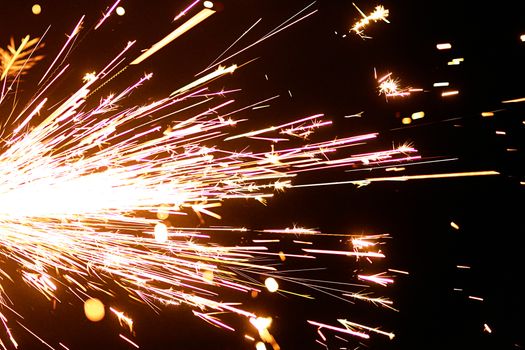 Dazzling close-up of a sparkler emitting bright sparks on a dark background.