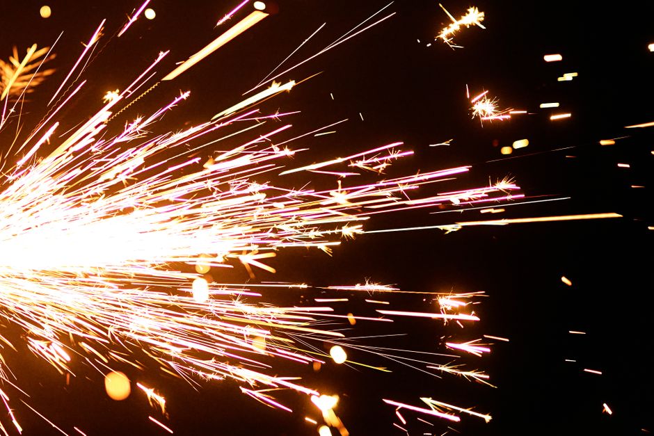 Dazzling close-up of a sparkler emitting bright sparks on a dark background.