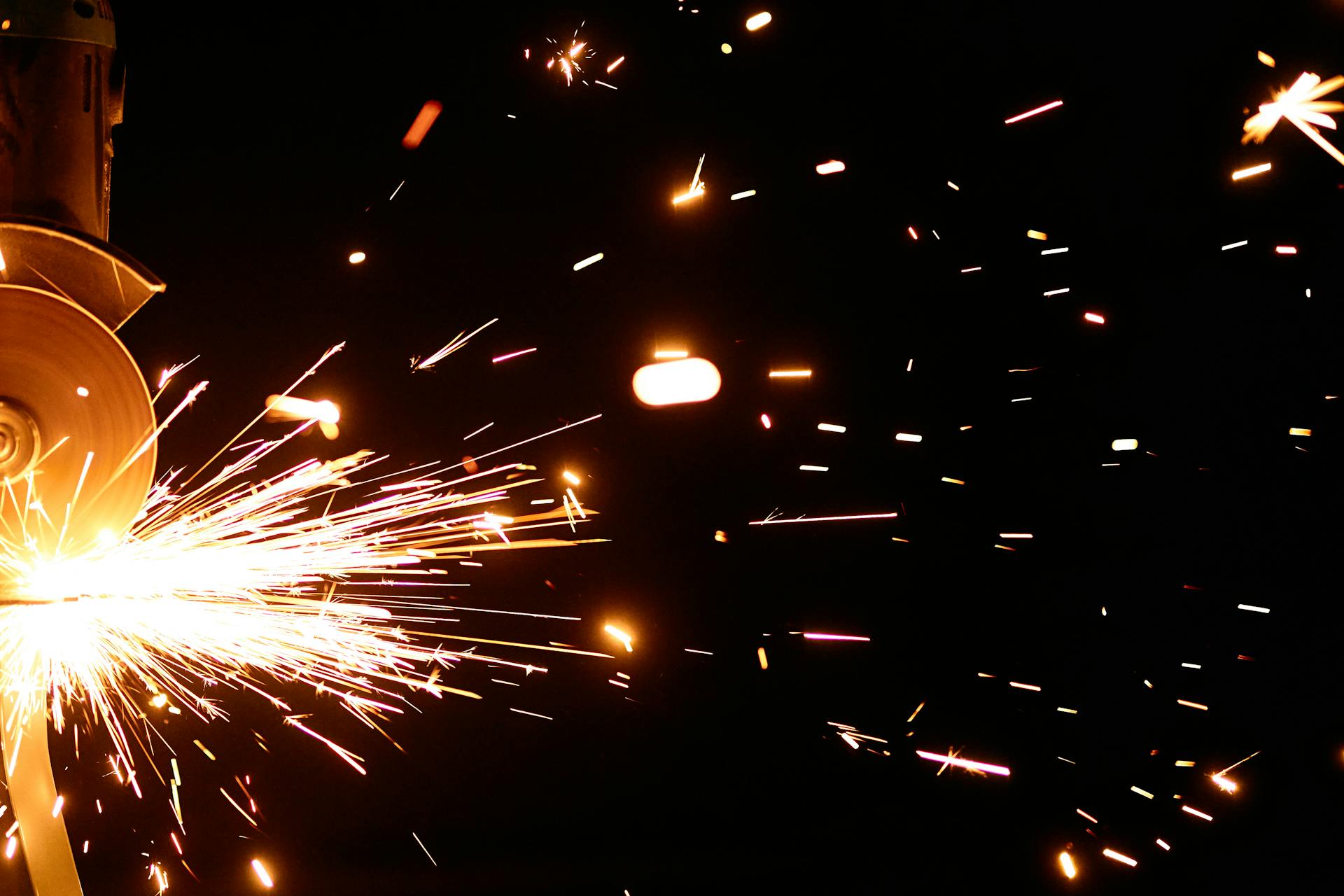 Close-up of vibrant sparks from an angle grinder against a dark background.