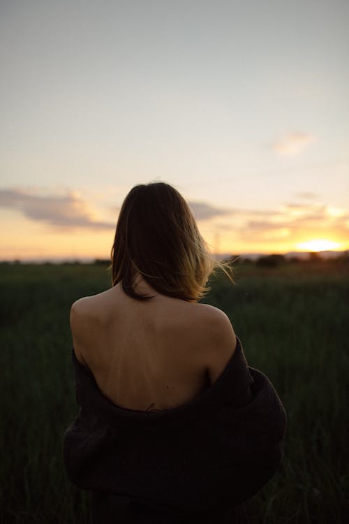 Young girl standing back on meadow at sunset