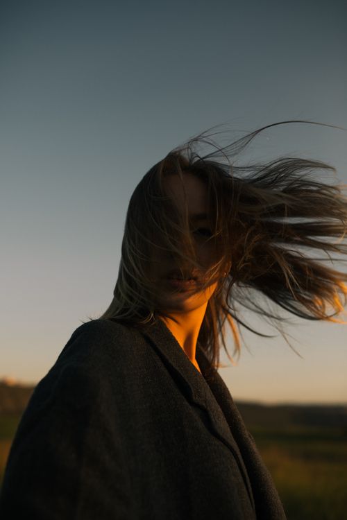 Free Caucasian woman with long hair in coat at sunset, wind in hair. Stock Photo