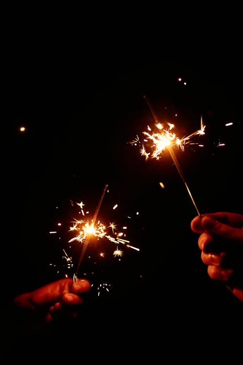 Two People Holding Burning Sparklers in the Dark