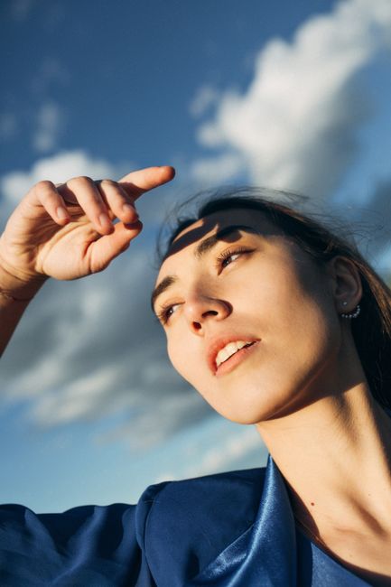 Close-up portrait of a young woman in sunlight with a thoughtful expression and clear blue sky.