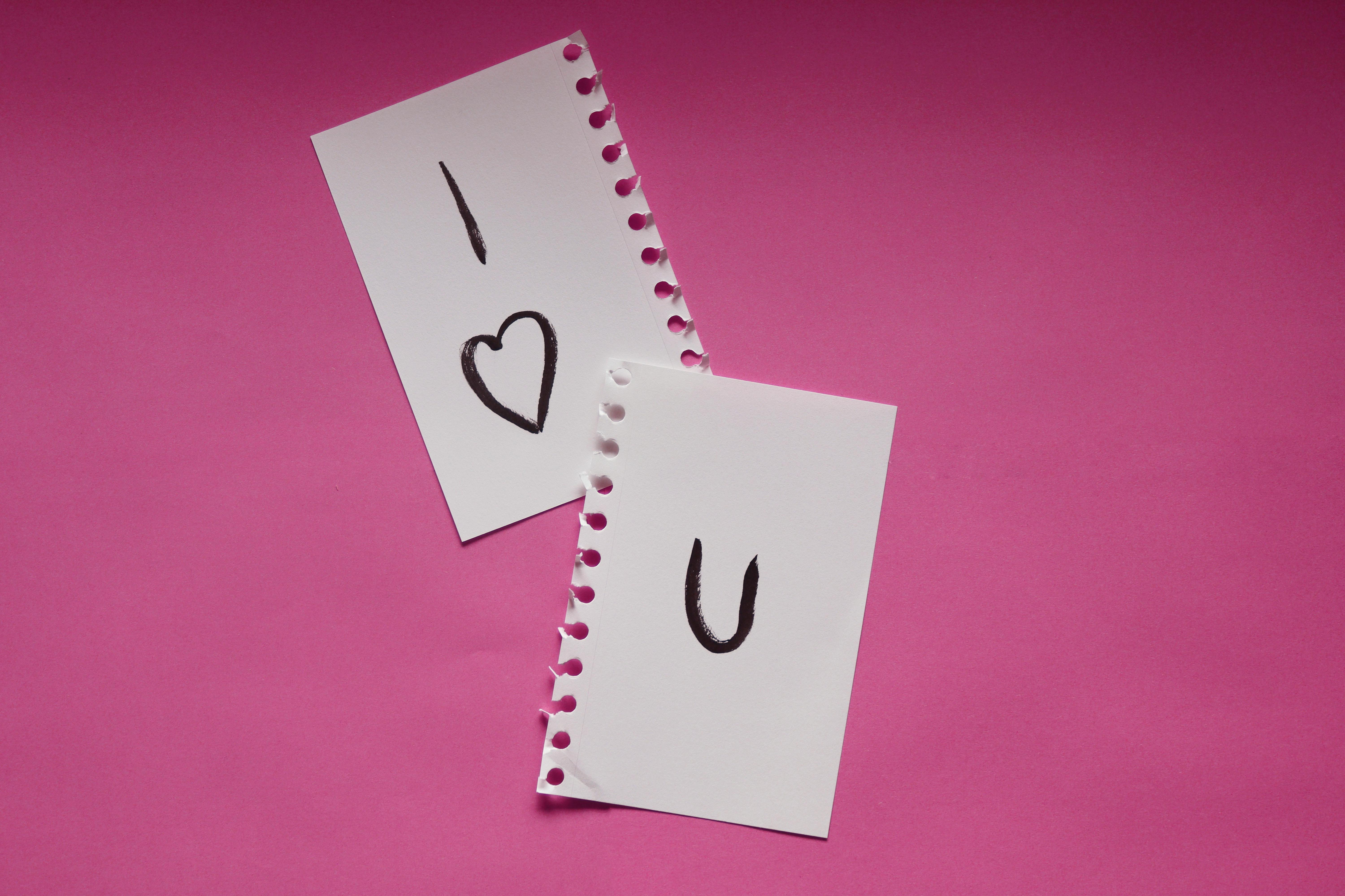 Two torn pieces of paper on pink background with 'I Love U' message.