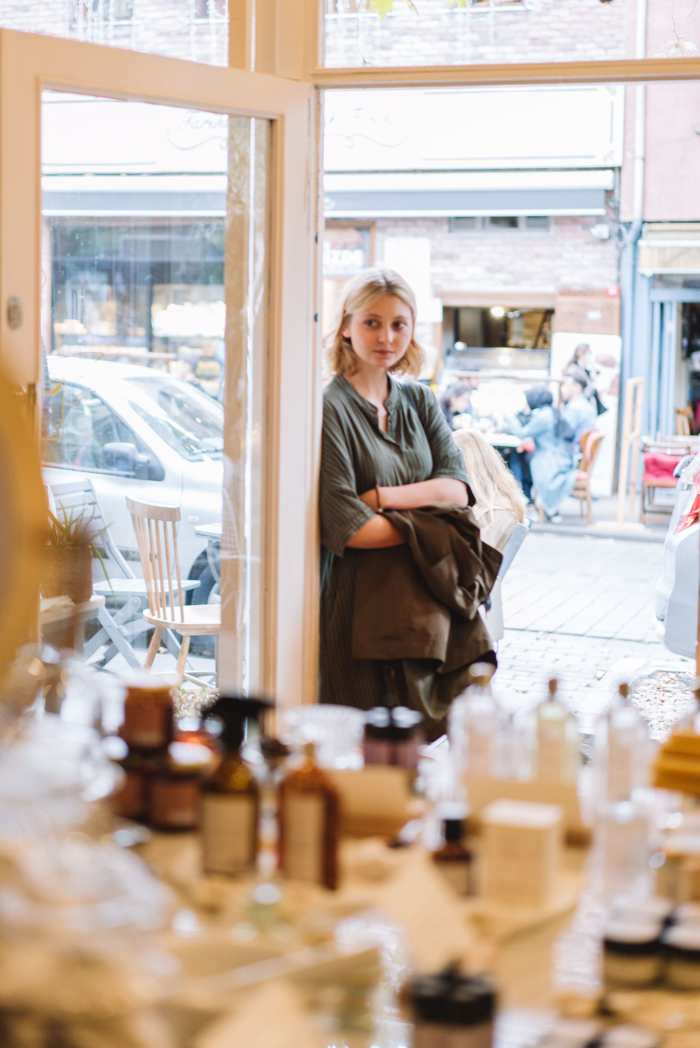 A young woman stands at a shop window, gazing inside thoughtfully.