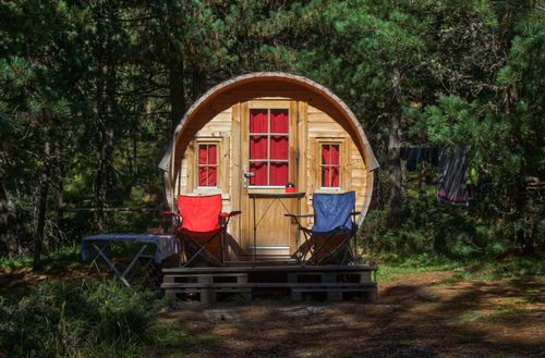 Free Charming rustic wooden cabin in a tranquil forest with red and blue camping chairs. Stock Photo