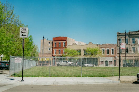 A street view in Chicago showing a vacant lot with surrounding buildings and clear blue sky.