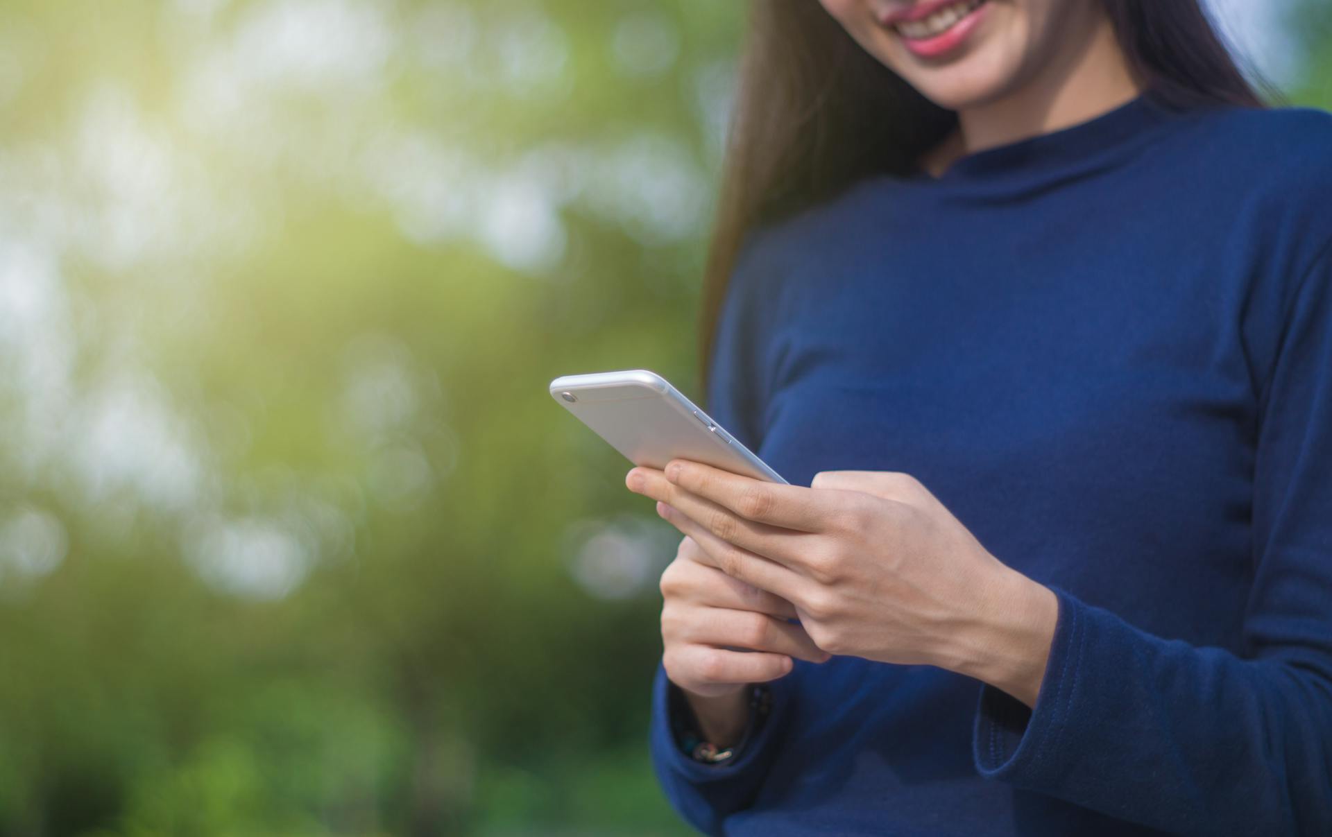 A woman using a smartphone outdoors, conveying positive emotions and modern technology in nature.