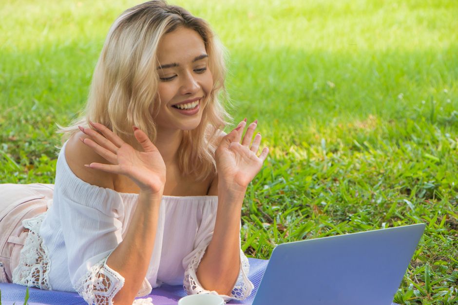 How Hybrid Mattresses Alleviate Back Pain for Chronic Sufferers Young woman in grass making a video call, smiling and waving at the laptop camera.