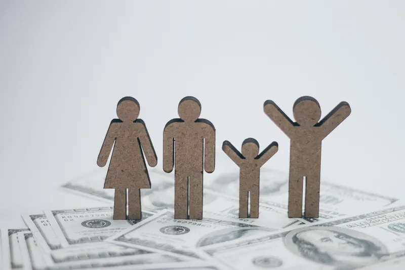 Wooden family figures standing on dollar bills — illustrating a home budget
