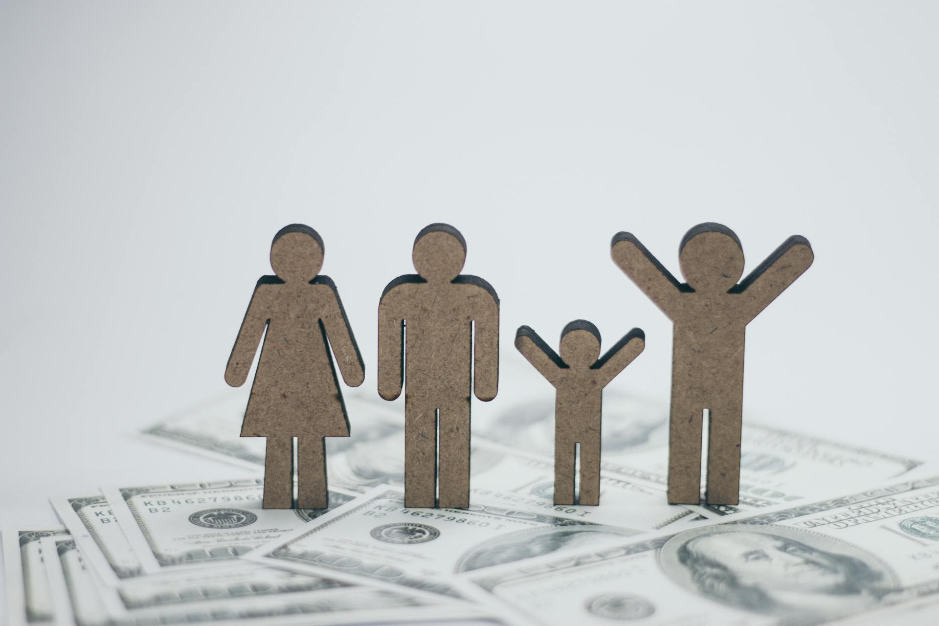 Wooden family figurines on dollar bills symbolizing financial stability.