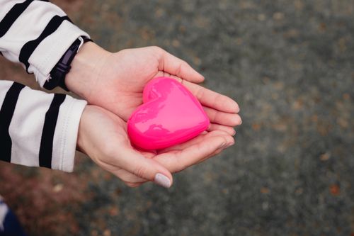 Free Close-up of hands holding a pink heart-shaped toy outdoors, symbolizing love and care. Stock Photo