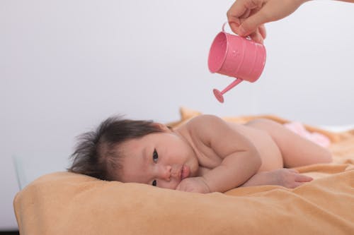Topless Baby Lying on Bed Holding Red Plastic Cup