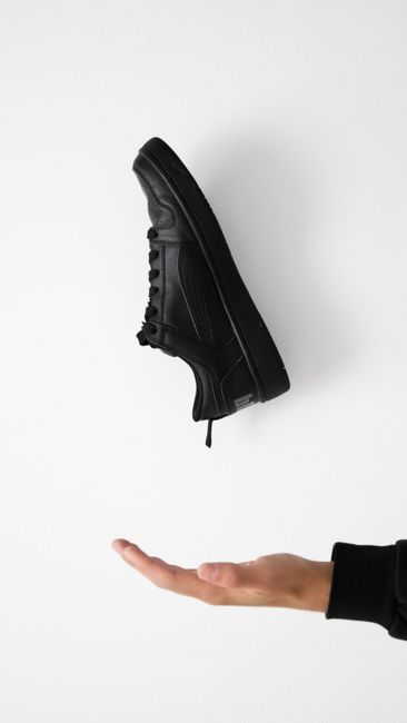 Fotomural Imagen minimalista de una zapatilla negra flotando sobre una mano en fondo blanco.