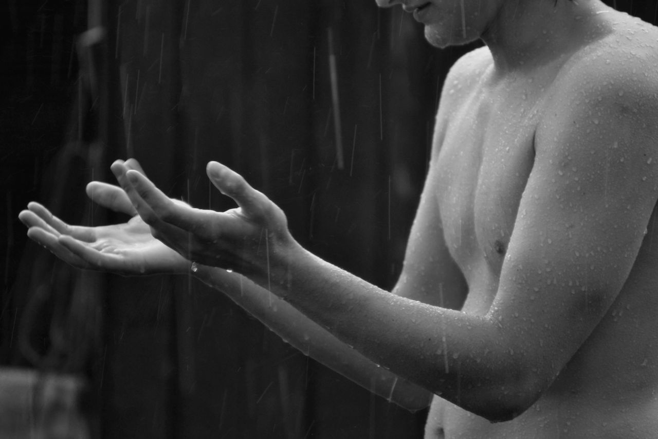 black and white image of shirtless man embracing rain