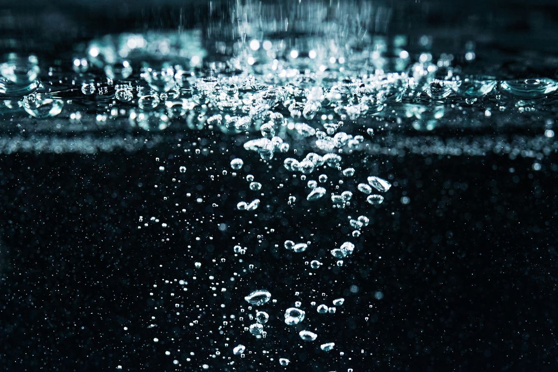 Close-up of fine bubbles rising through clear water against a dark background