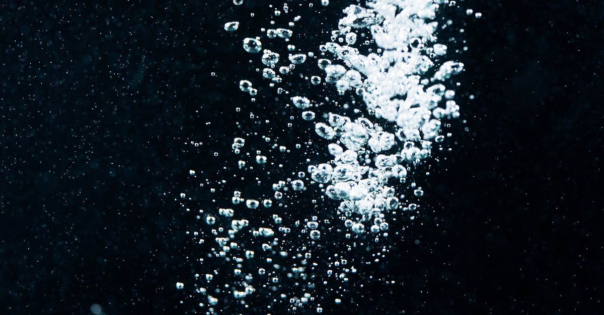 A close-up of effervescent water bubbles rising in a dark liquid, creating a vibrant and dynamic visual.